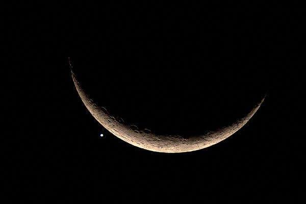 A crescent moon in the night sky with a bright dot at its edge.