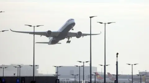 Getty Images A plane takes off over Heathrow airport. Buildings can be seen in the background and other planes are parked alongside them 