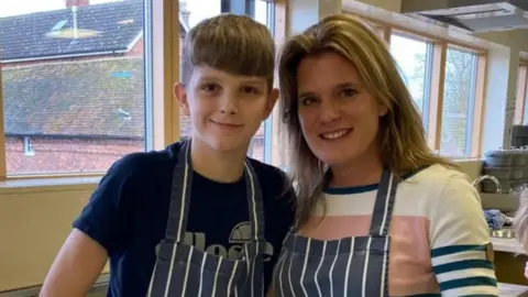 Ellen Roome A woman stands with a young boy. They are both wearing aprons and are smiling.